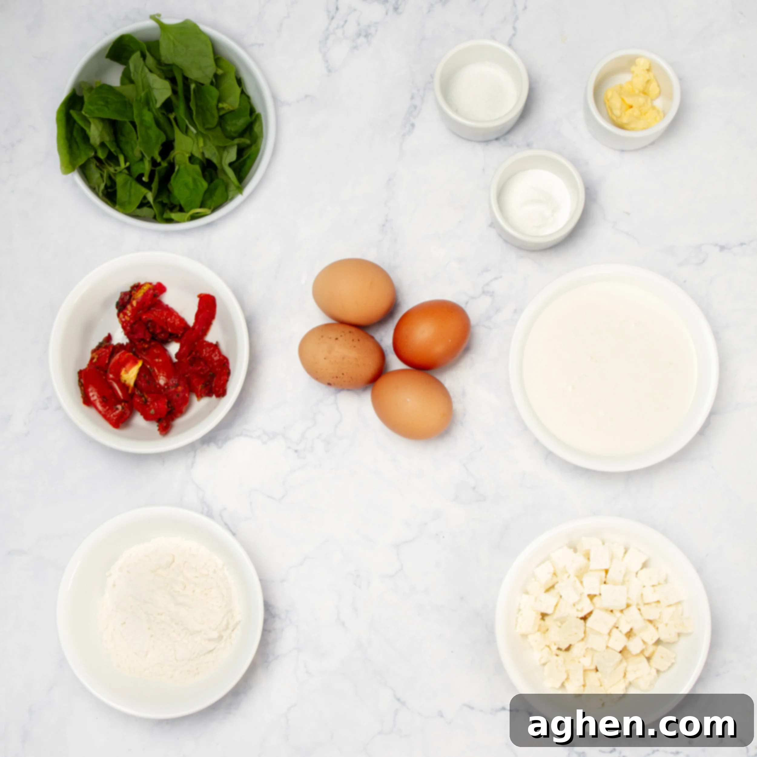 All the fresh ingredients for Spinach, Feta, and Sun-Dried Tomato Muffins are neatly arranged in separate glass and ceramic dishes on a clean kitchen counter, showcasing vibrant colors and textures, ready for the baking process.