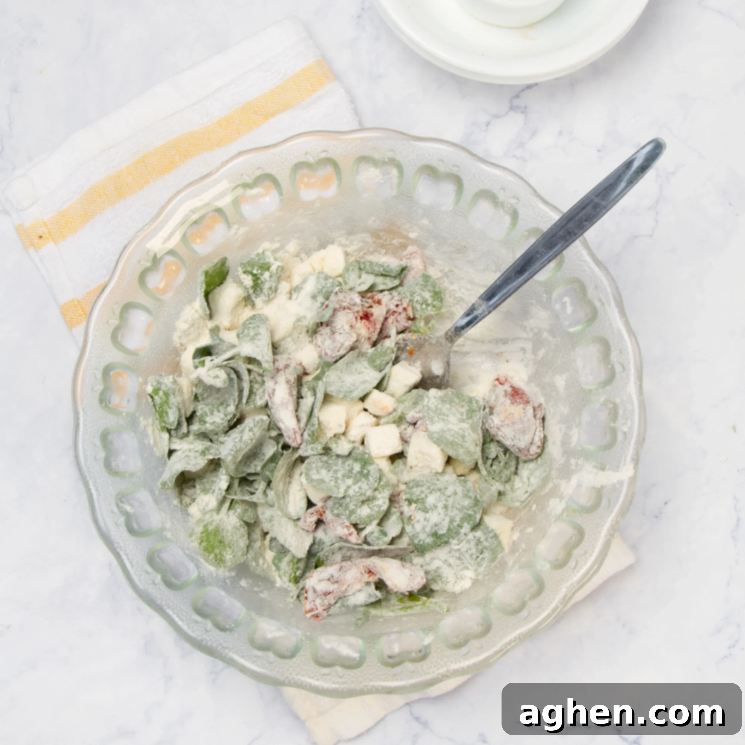 The bowl of crumbled feta, fresh spinach, and sun-dried tomatoes now has a fine dusting of flour mixture, which has been gently tossed to coat the ingredients evenly, preparing them for the addition of wet components.