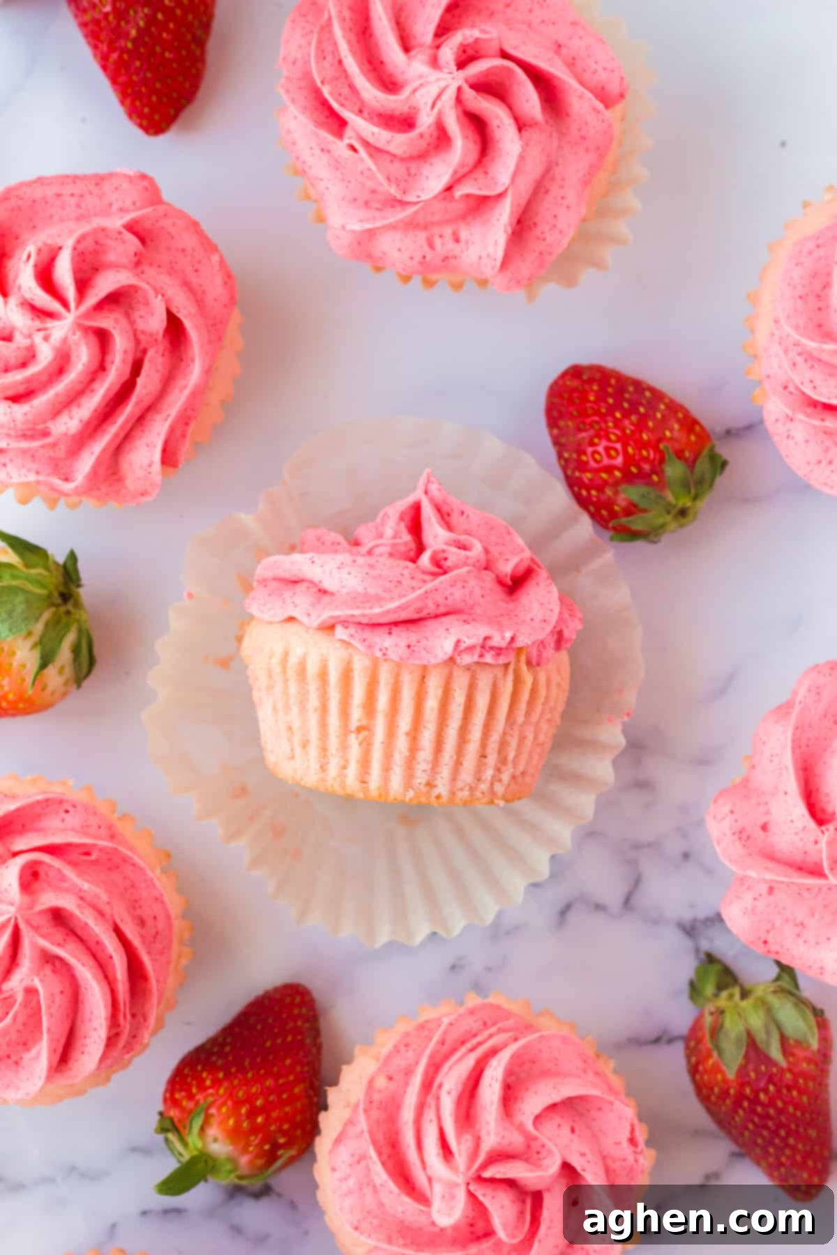 Strawberry Filled Cupcakes with Strawberry Jello Buttercream on marble countertop with fresh strawberries around them.