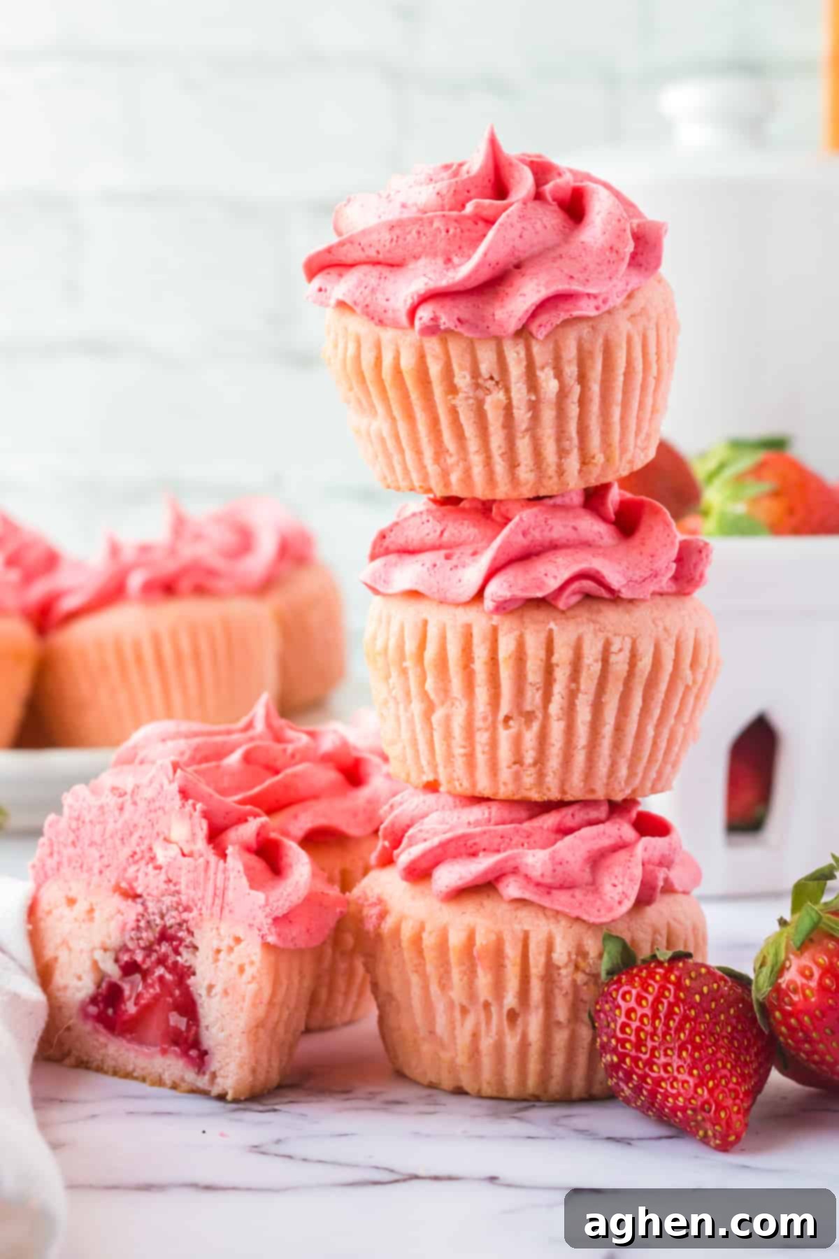 3 strawberry cupcakes stacked on top of one another with another cupcake cut in half next to show strawberry in center
