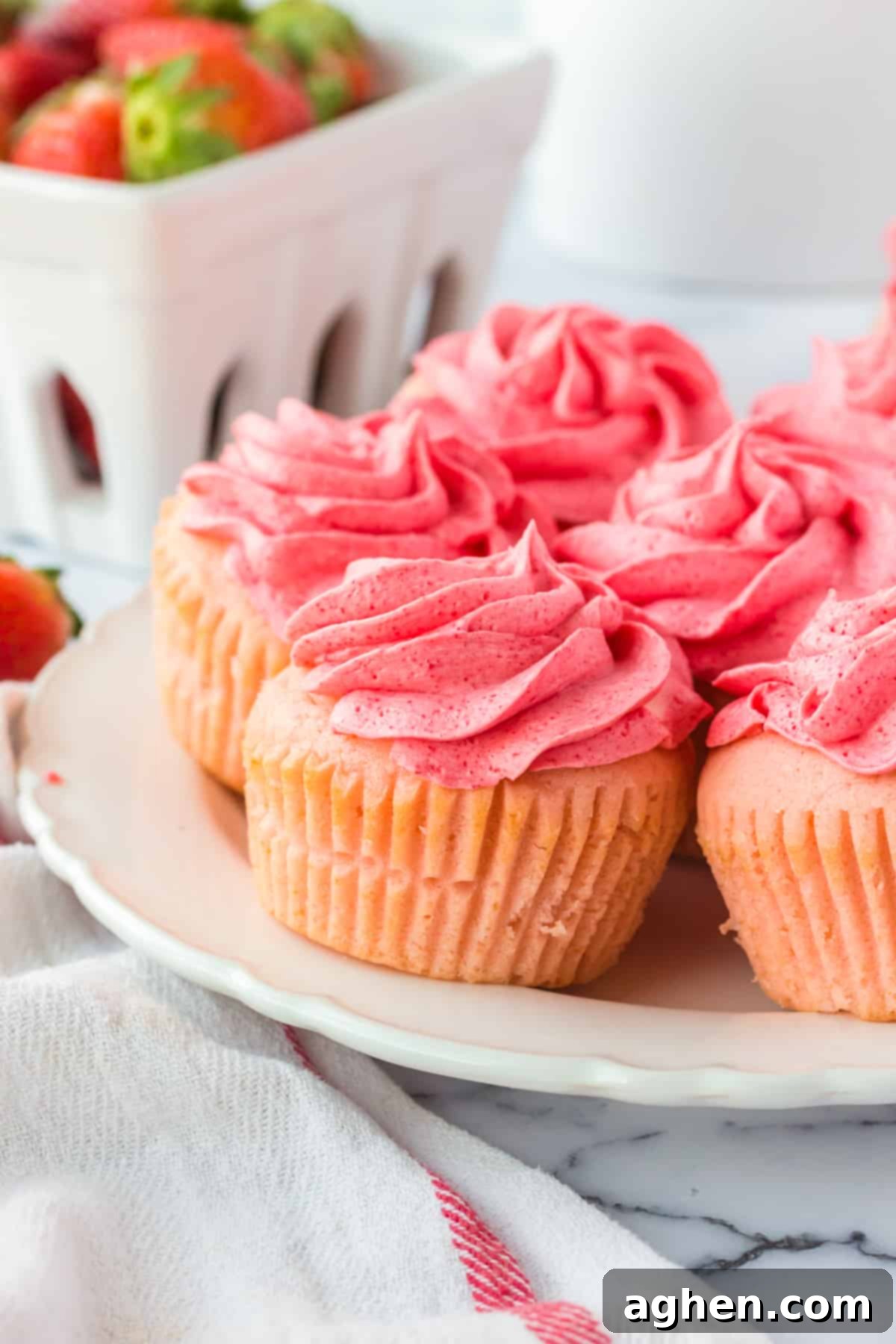 Pink frosted cupcakes with fresh strawberries in the background