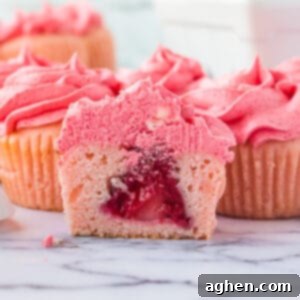 Pink cupcake with pink frosting sliced in half to show whole strawberry in the center.