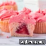 Pink cupcake with pink frosting sliced in half to show whole strawberry in the center.