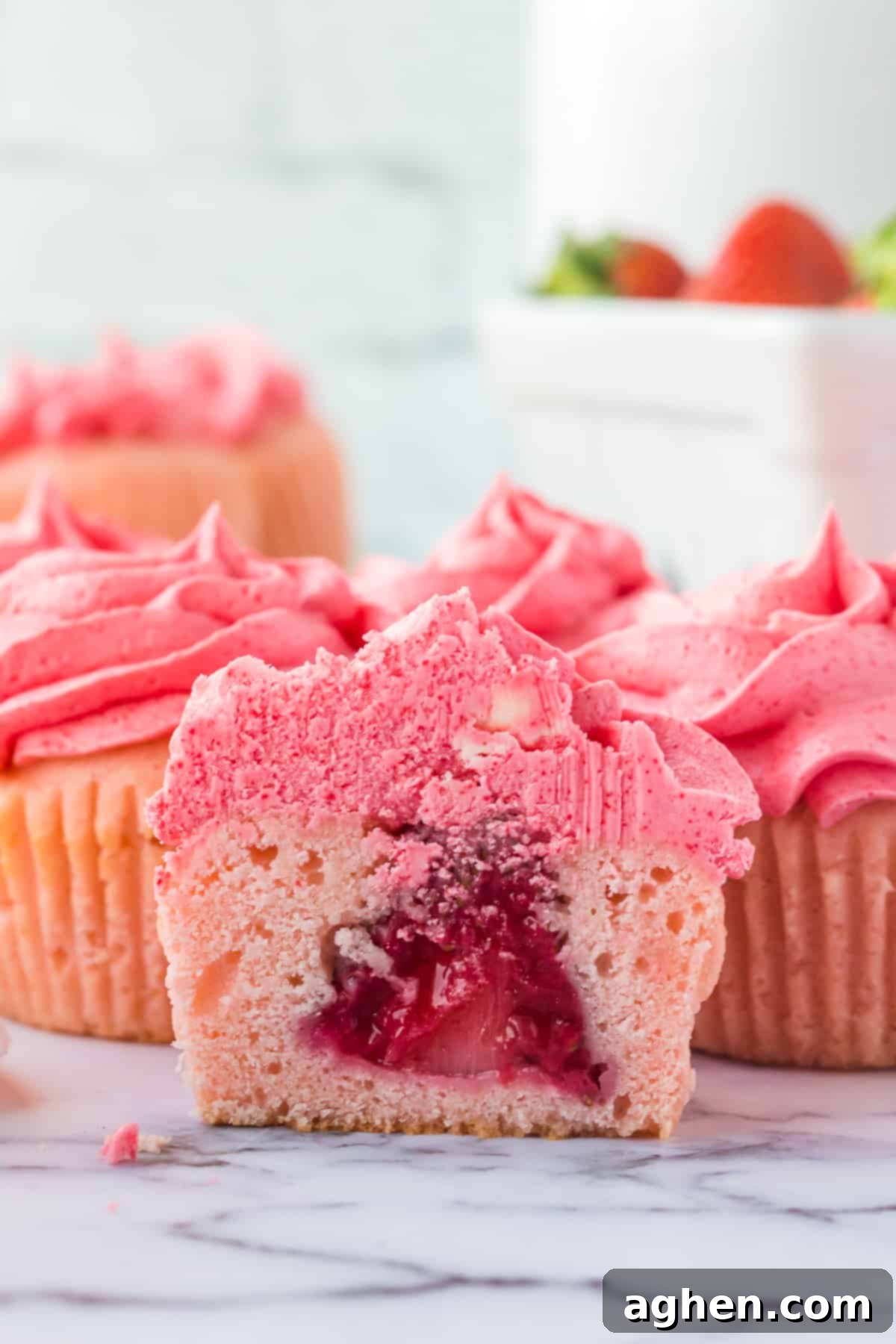 Pink cupcake with pink frosting sliced in half to show whole strawberry in the center.