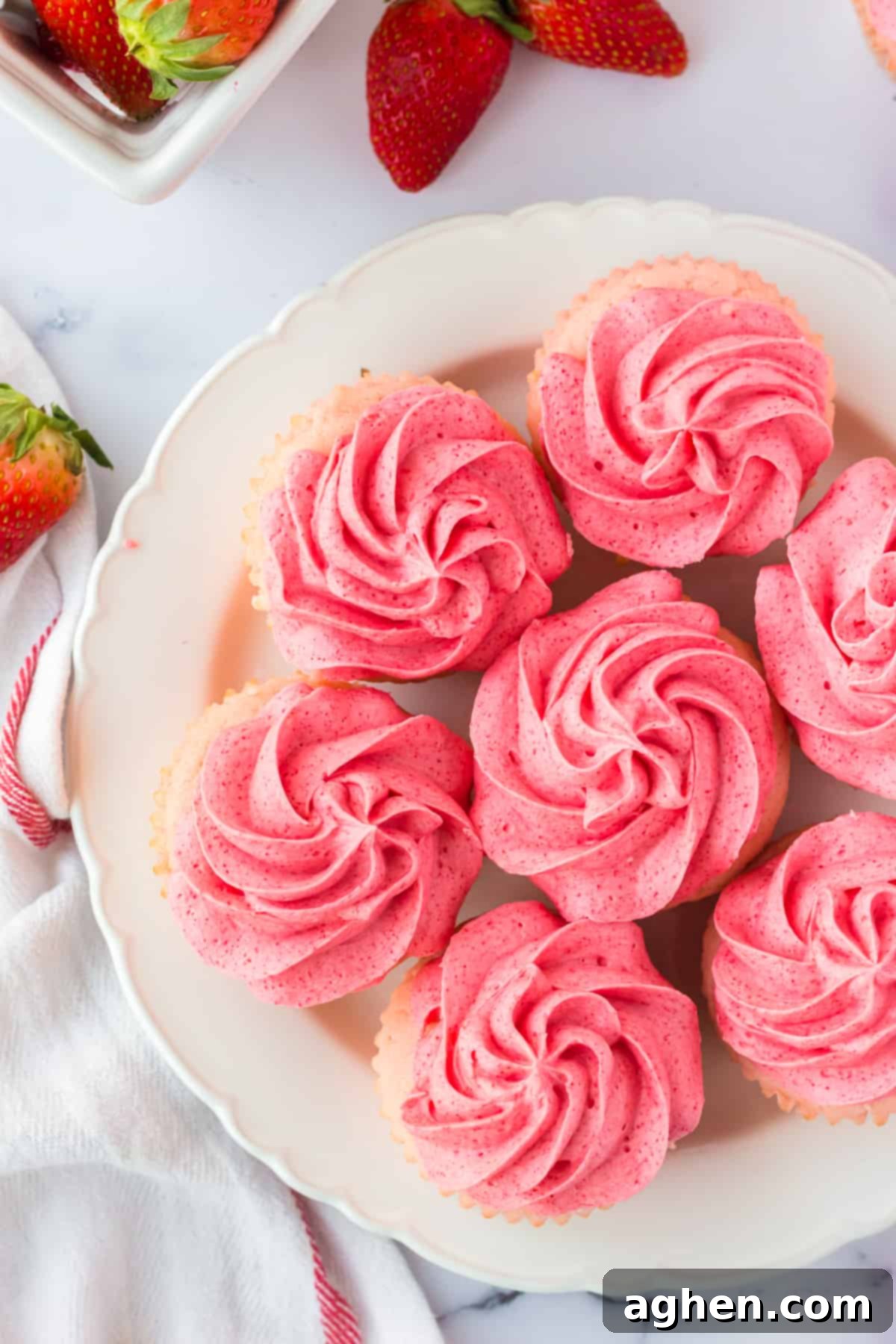 cupcakes with pink frosting arranged in a circle on white plate with strawberries in background