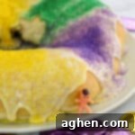 King cake with glaze and green, yellow, and purple sanding sugars. A small toy baby is leaning on the cake.