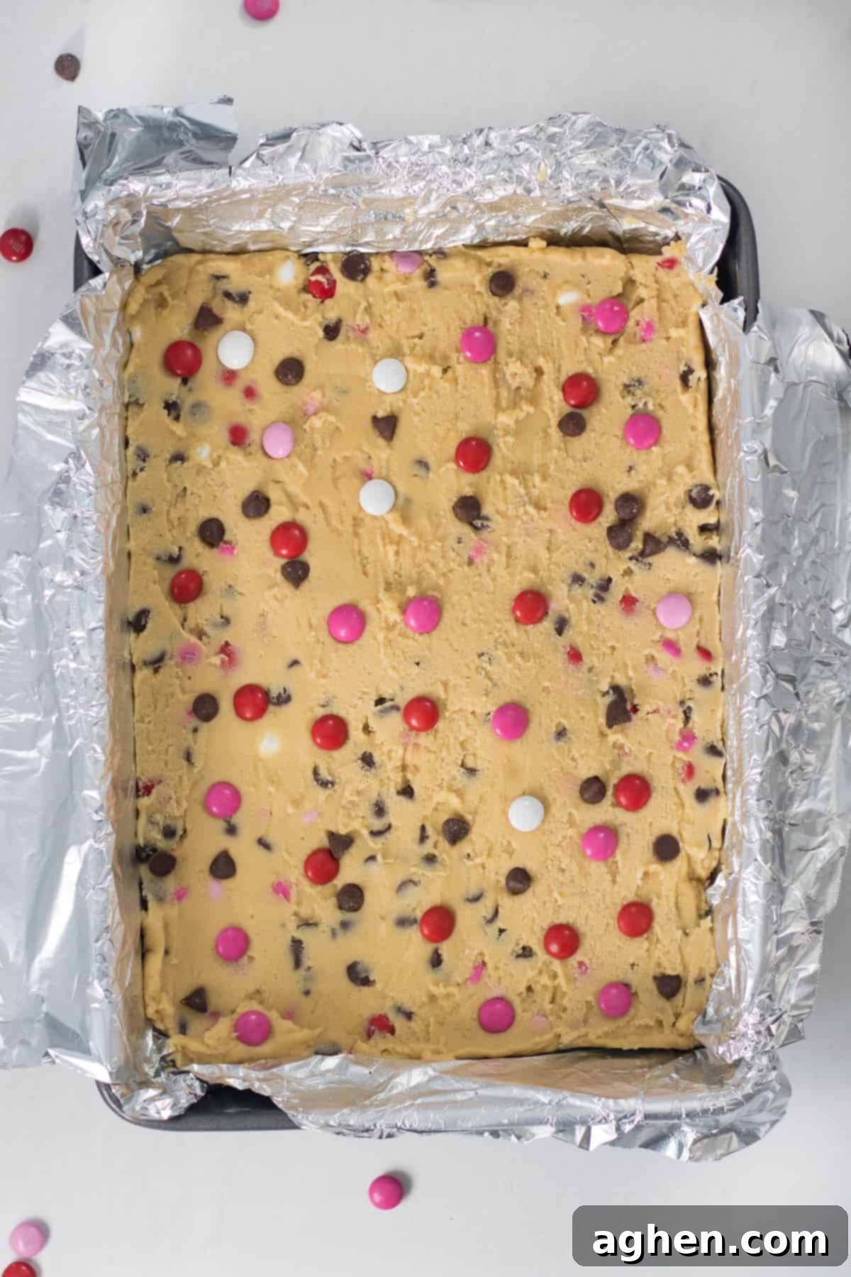 Sweetheart Cookie Squares 7 Unbaked Valentine's Day cookie bar dough spread evenly in a baking pan, topped with extra M&Ms and chocolate chips, ready for the oven.
