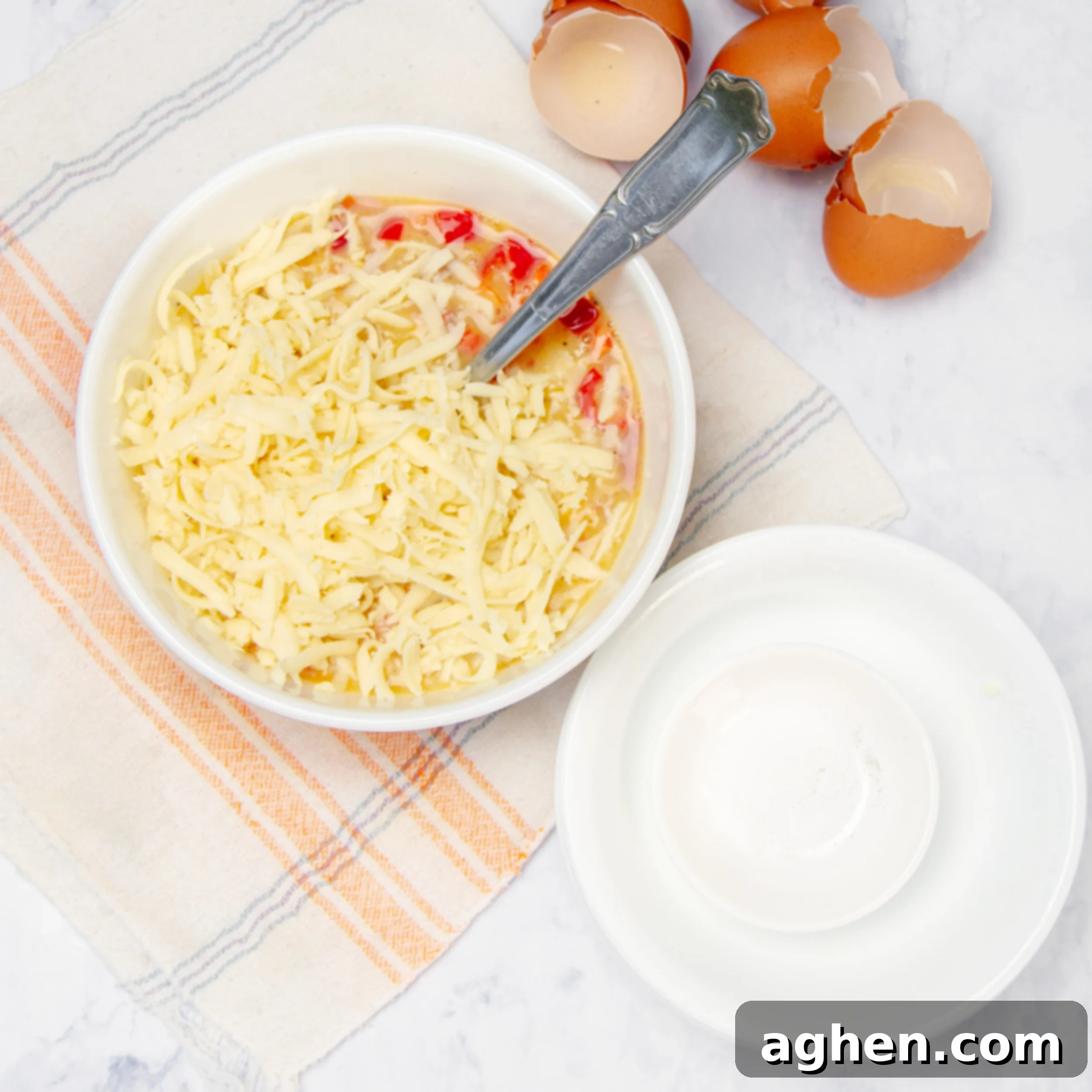 A colorful egg mixture in a bowl, with diced red bell pepper, smoked turkey ham, shredded cheddar cheese, salt, and pepper clearly visible and mixed in.