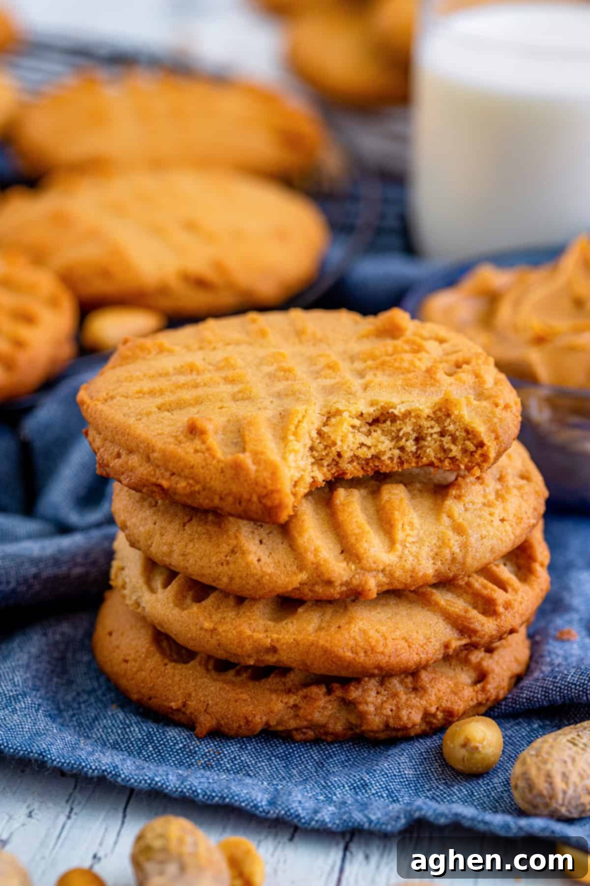 Old-fashioned peanut butter cookies with characteristic fork prong lattice on top. One cookie has a bite taken out of it to show the crisp yet soft texture, evoking grandma's baking.