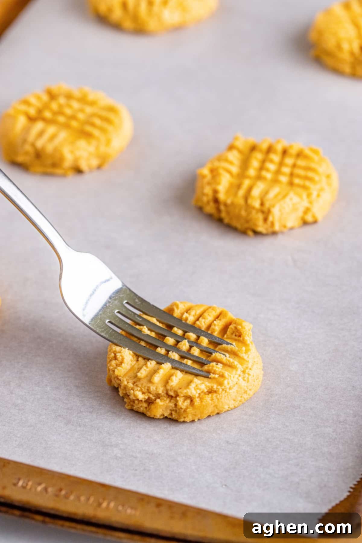 A fork gently pressing down on peanut butter cookie dough to create the signature criss-cross pattern before baking, demonstrating Step 5.