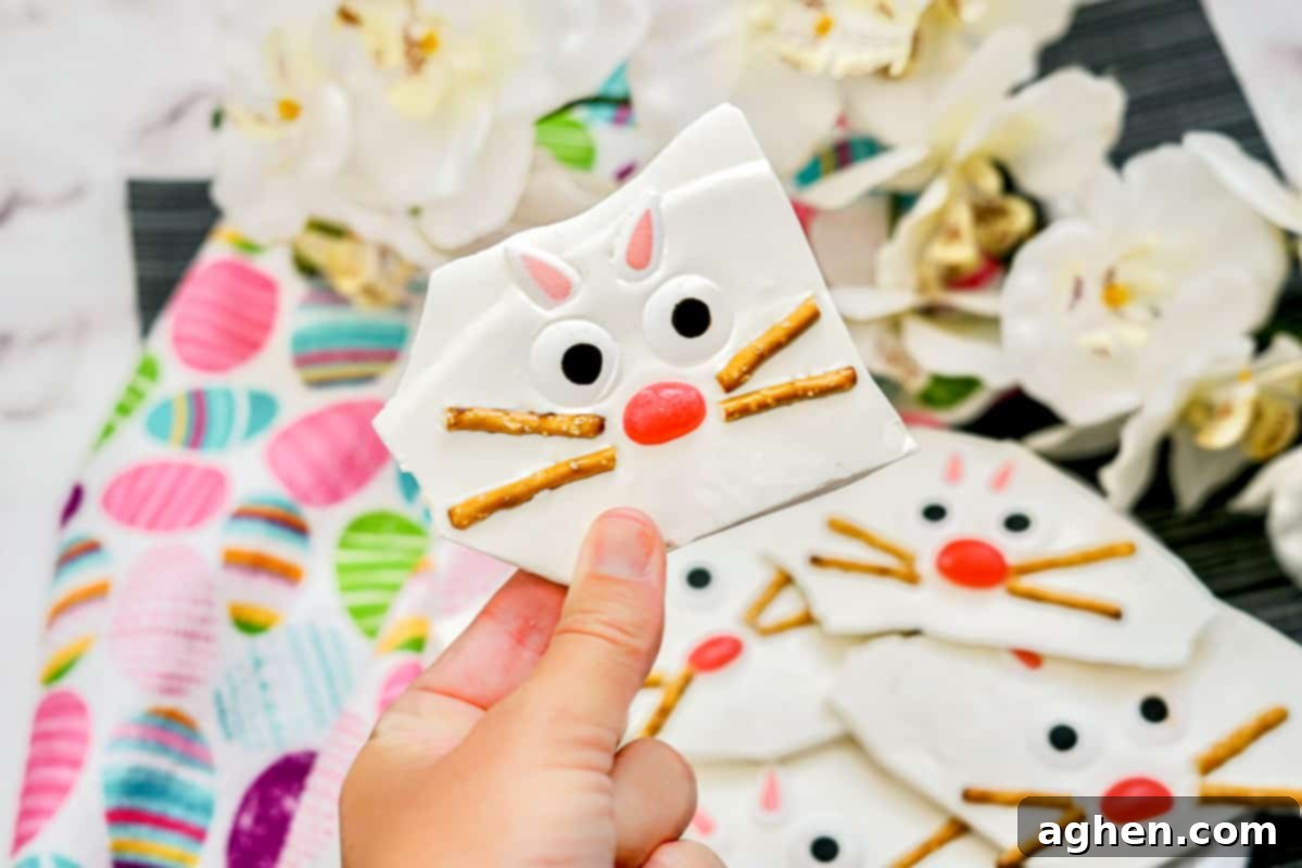 Hand holding a piece of Easter bark with a bunny face made from pretzel sticks, jelly beans, candy ears, and candy eyes.