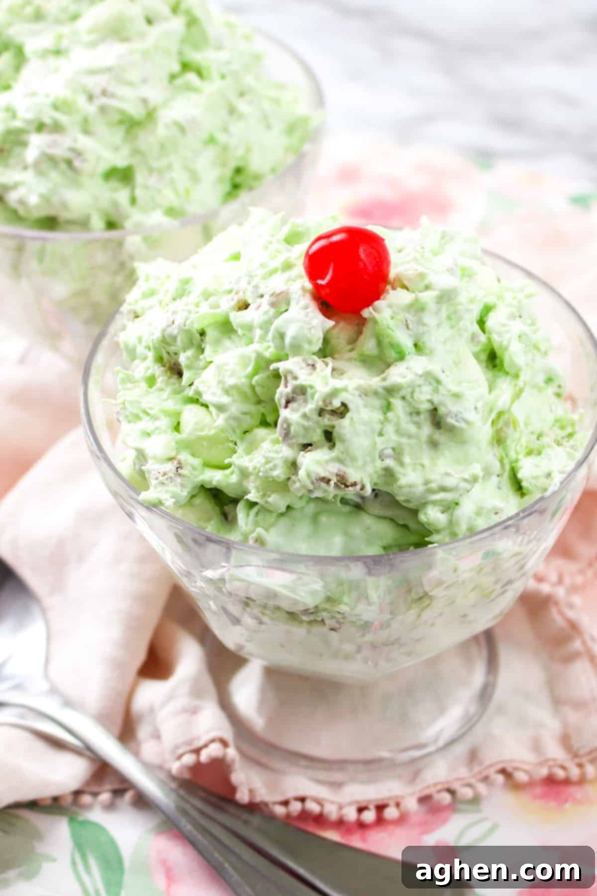 Watergate salad in a elegant serving glass, garnished with a cherry and a sprig of mint.
