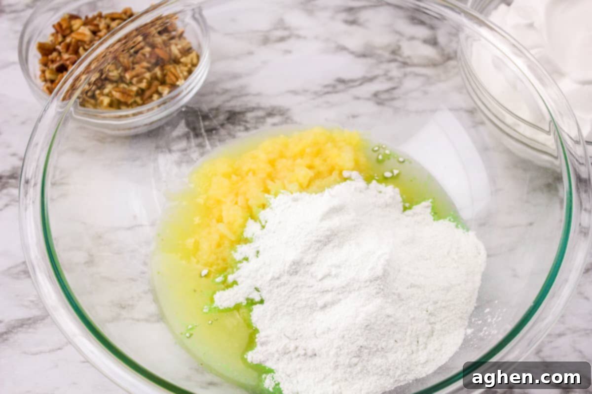 Crushed pineapple and pistachio pudding mix being stirred together in a clear glass mixing bowl.