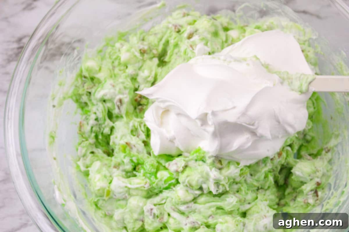 Pistachio salad mixture with a generous dollop of Cool Whip on top, ready to be folded in.