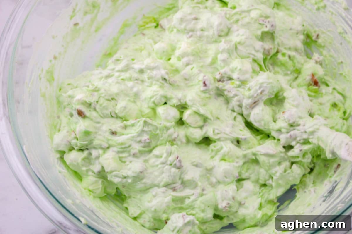 A large glass bowl filled with the finished pistachio delight dessert salad, showing its fluffy texture and green color.