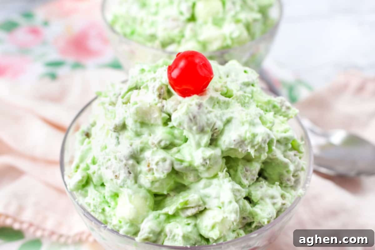 A close-up shot of Watergate Salad in a glass bowl, topped with pecans, cool whip, pineapple chunks, and a cherry.