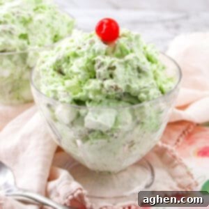 Watergate salad in a glass bowl topped with a cherry and mint.
