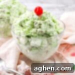Watergate salad in a glass bowl topped with a cherry and mint.