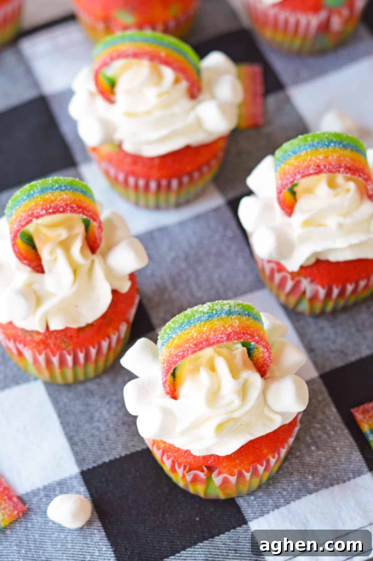 Four cupcakes decorated with rainbows, miniature marshmallows, and white frosting on top.