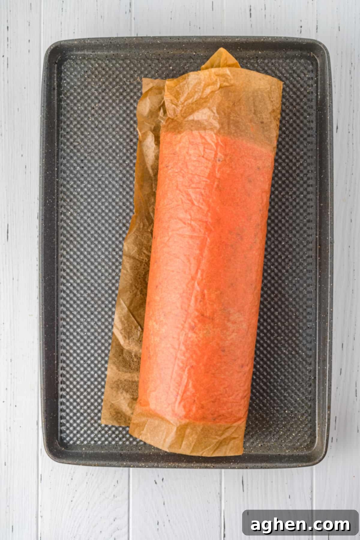 Cake rolled in parchment paper sitting on jelly roll pan.