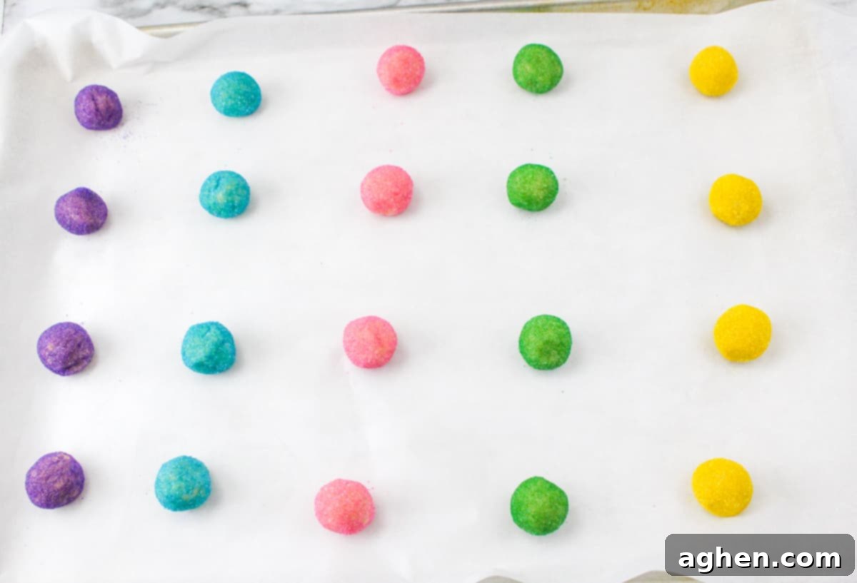 Purple, blue, pink, green, and yellow sugar-covered dough balls neatly arranged on a parchment-lined baking sheet.
