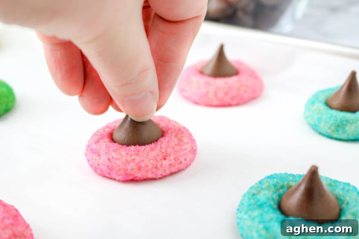 A hand pressing a Hershey's Kiss into the top of a warm, pink Easter Blossom Cookie.