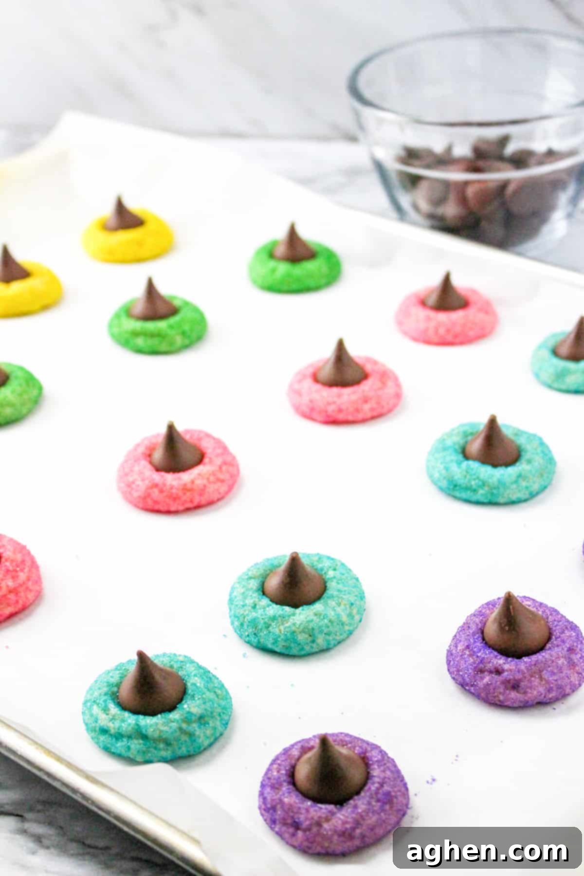 Easy Easter cookies with Hershey Kisses, featuring various pastel colors, on a lined baking sheet.