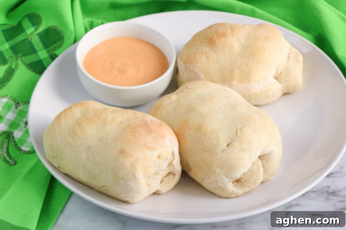 Golden-baked Reuben rolls made with pizza dough, served on a white plate with a small bowl of creamy Thousand Island dressing for dipping.