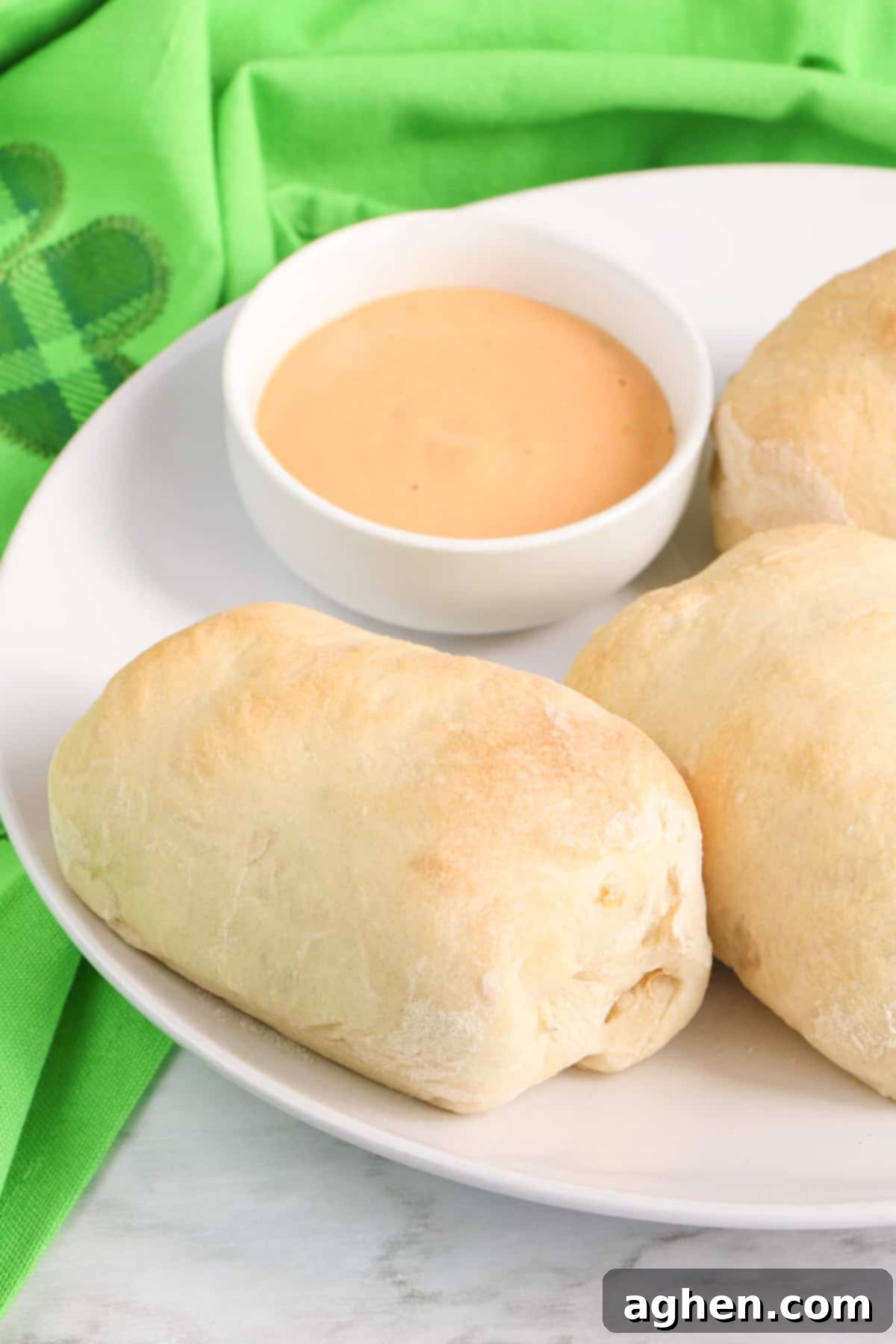 A single corned beef Reuben roll-up with a crispy pizza crust, presented on a white plate with a small ceramic bowl of Thousand Island dressing for dipping.