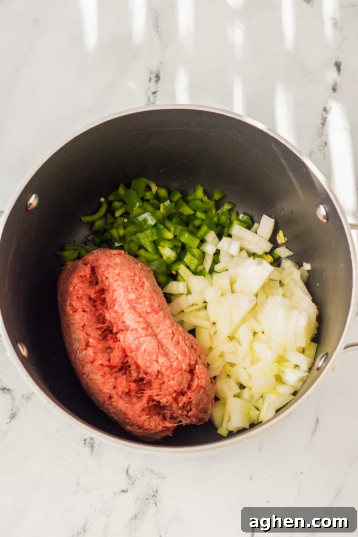Large pot with ground beef, diced onions, and diced green peppers.
