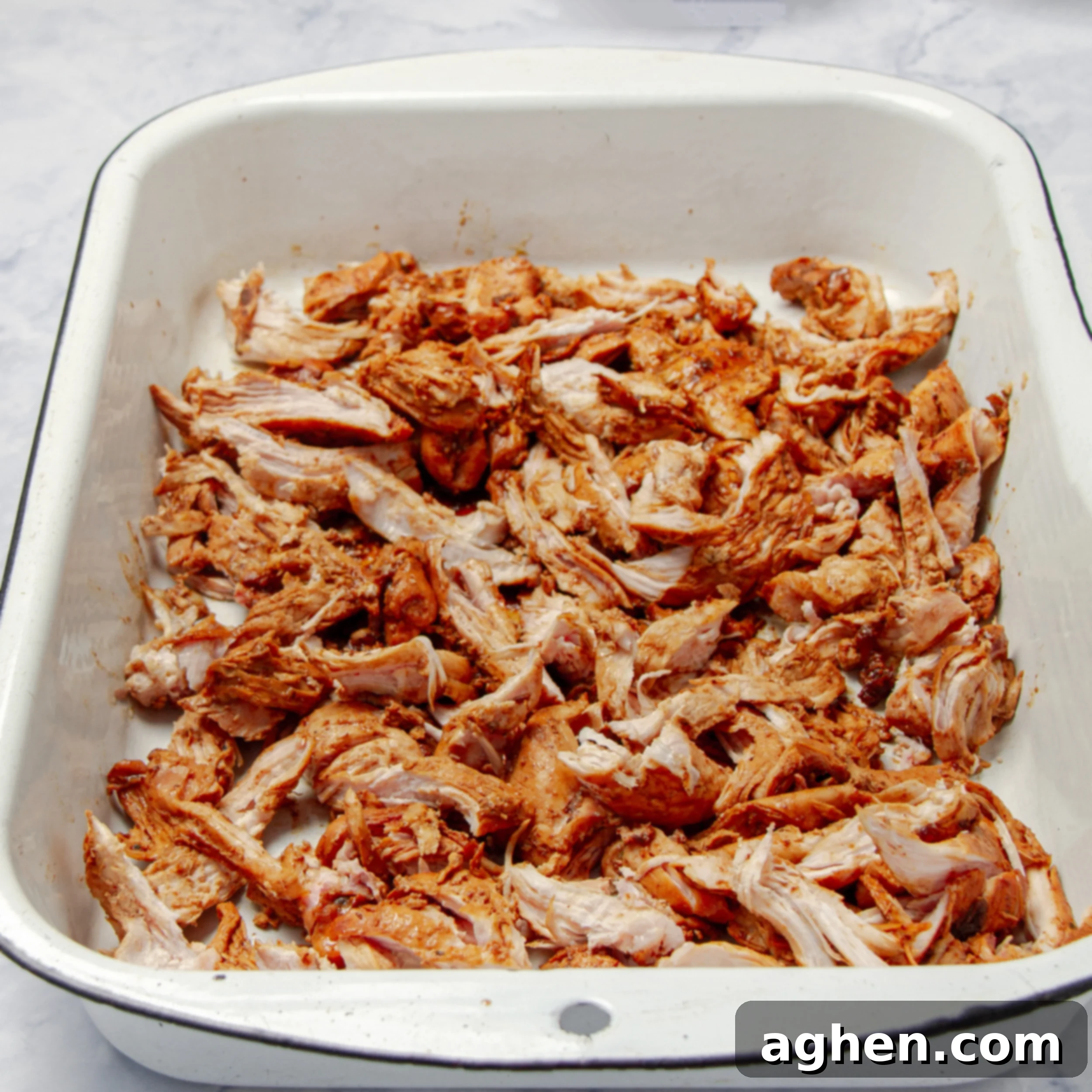 Shredded chicken spread on a parchment-lined baking sheet, drizzled with cooking liquid, before broiling.