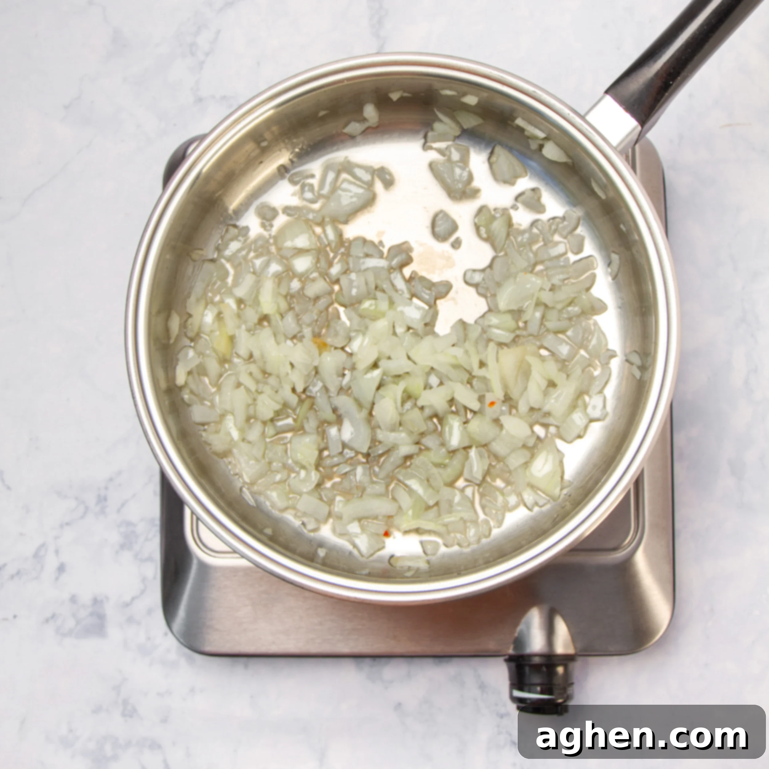 Diced white onions sautéing in olive oil in a large pan until translucent.