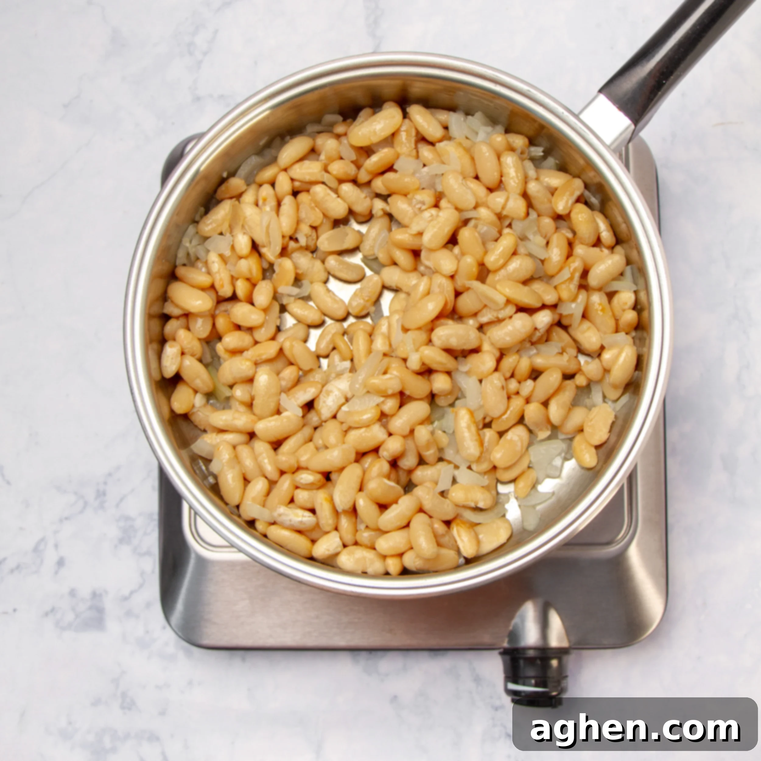 Cooked cannellini beans added to sautéed onions in a pan, ready for broth.