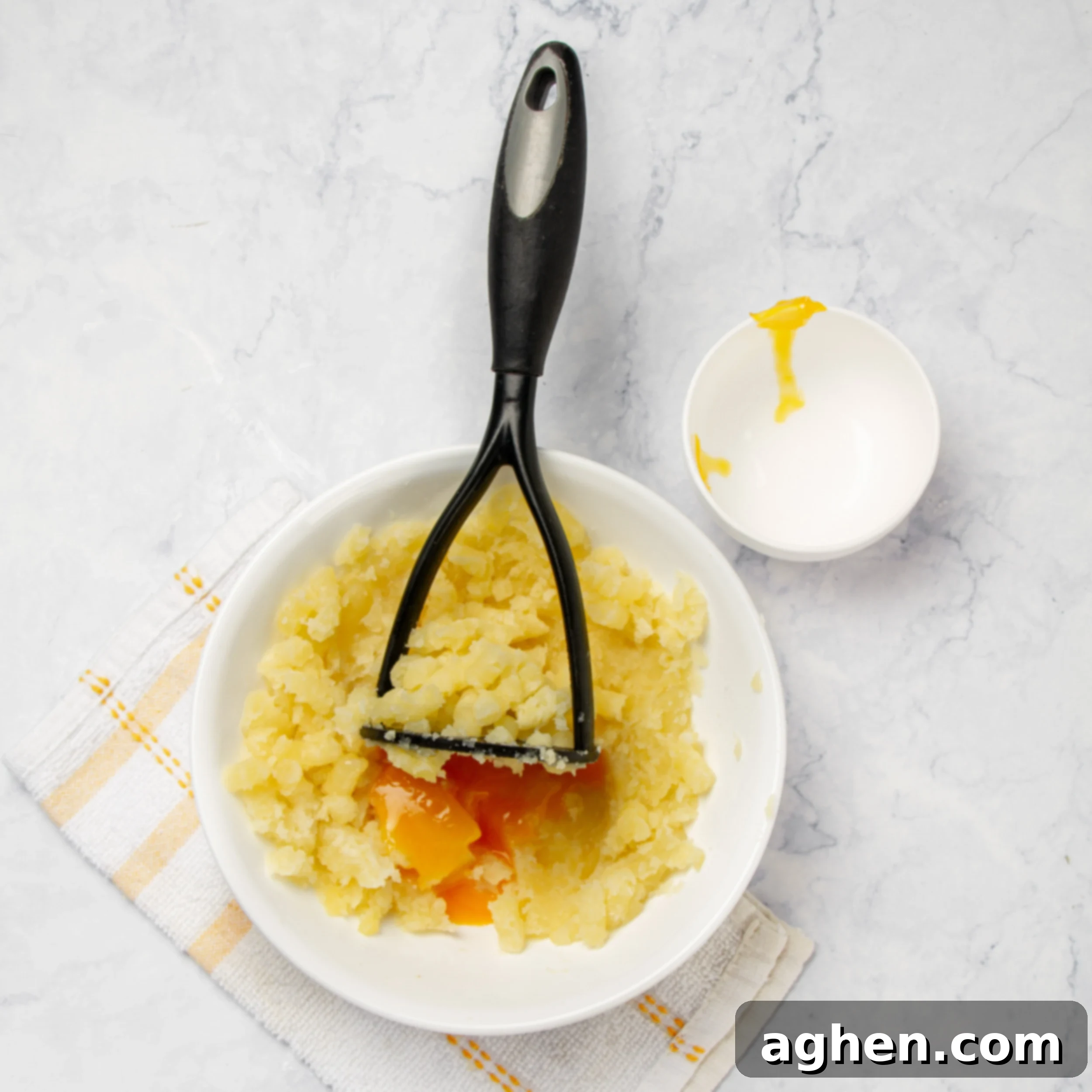 A hand mashing boiled potatoes in a bowl with a potato masher.
