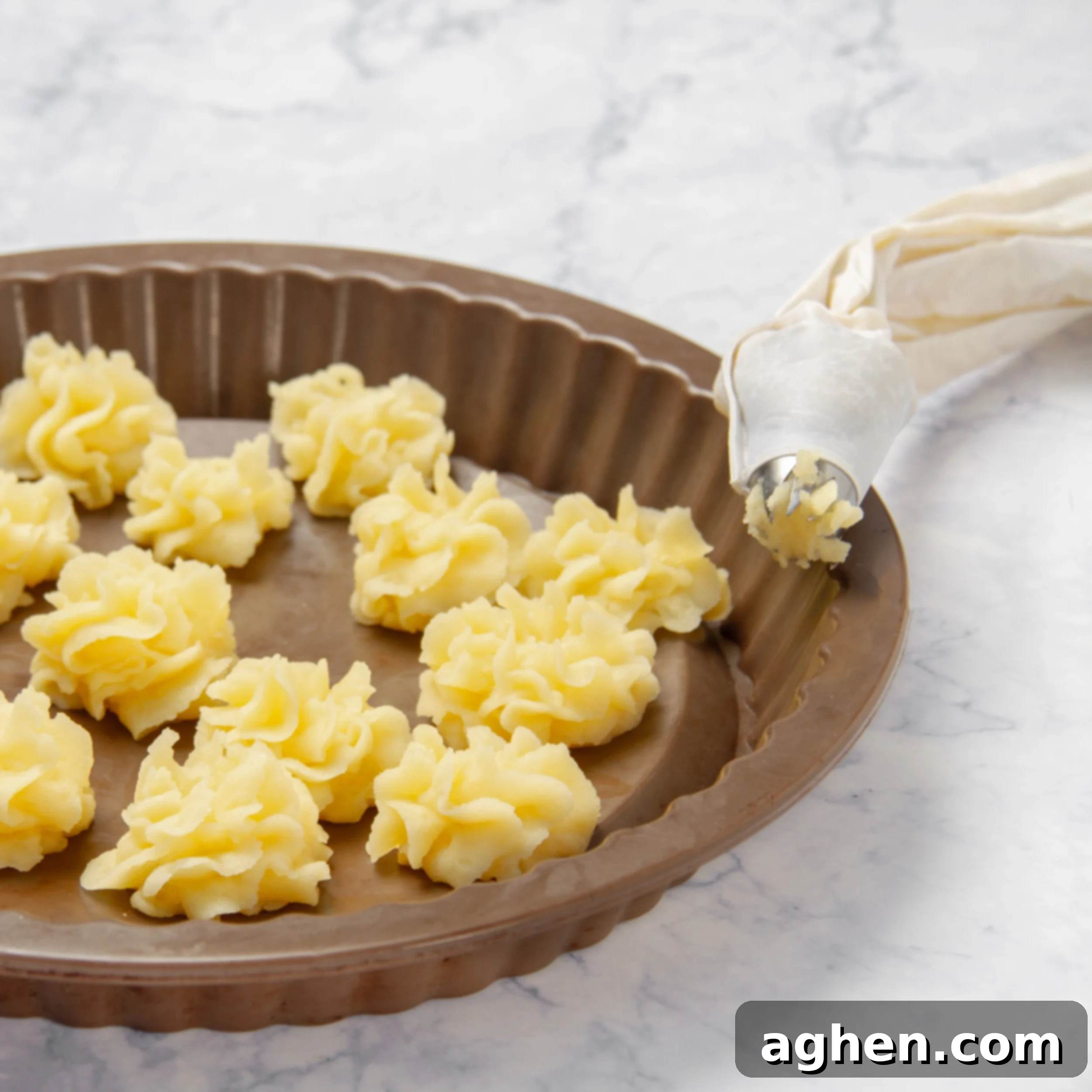 Mashed potatoes being piped onto a baking sheet, ready for the oven.