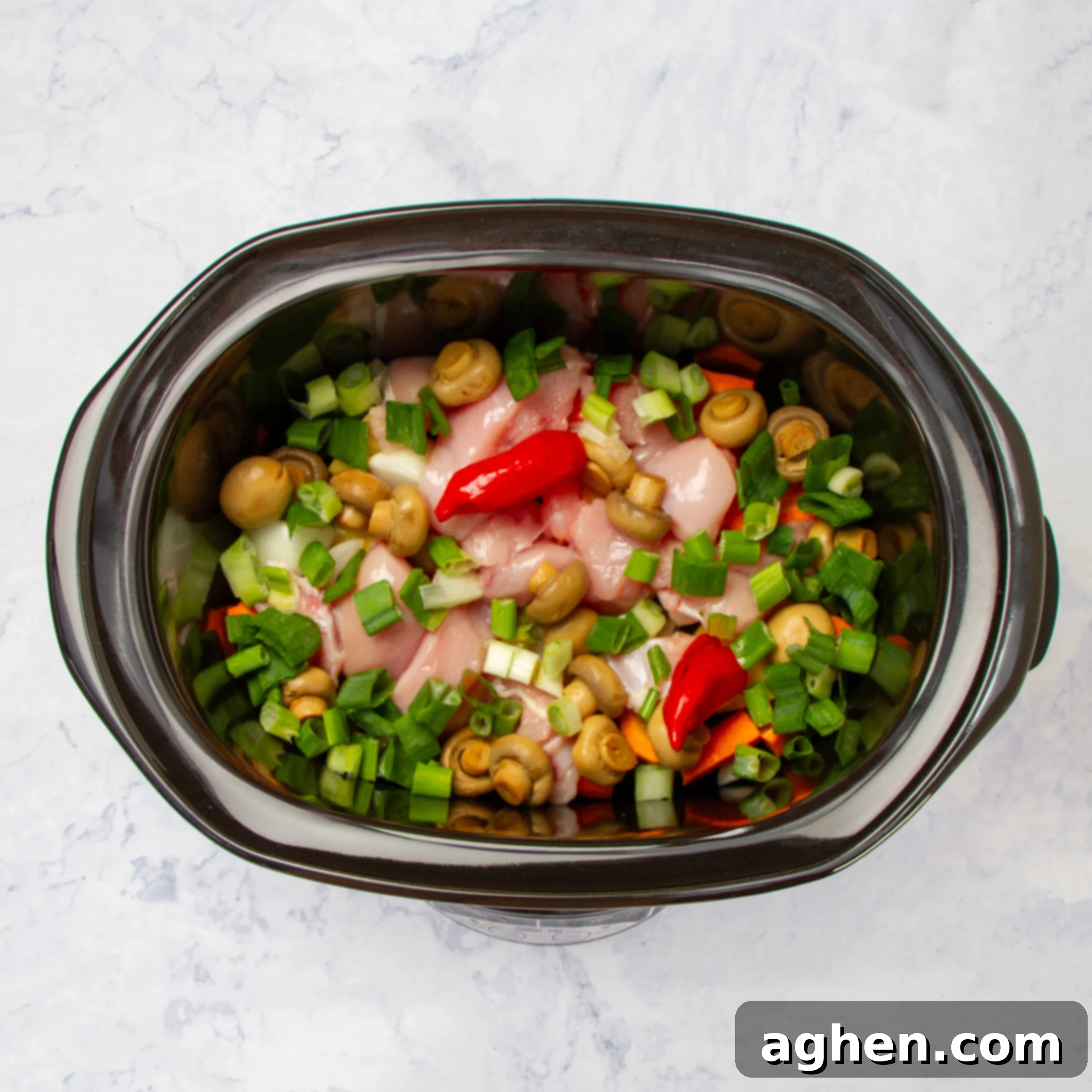 All ingredients assembled in the slow cooker, layered with vegetables at the bottom and chicken on top.