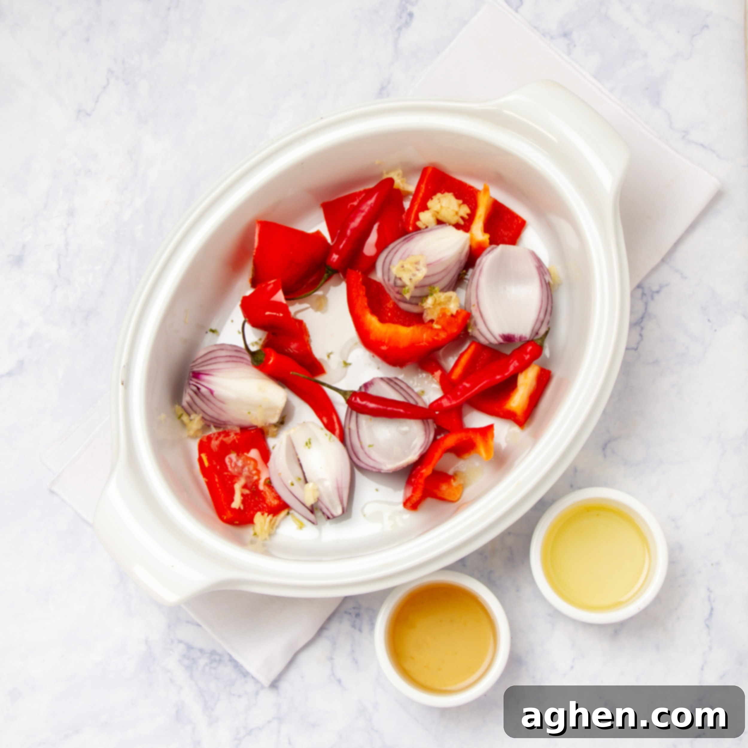 Red bell peppers, onions, garlic, and piri-piri chilies roasting on a baking sheet, part of the sauce preparation.