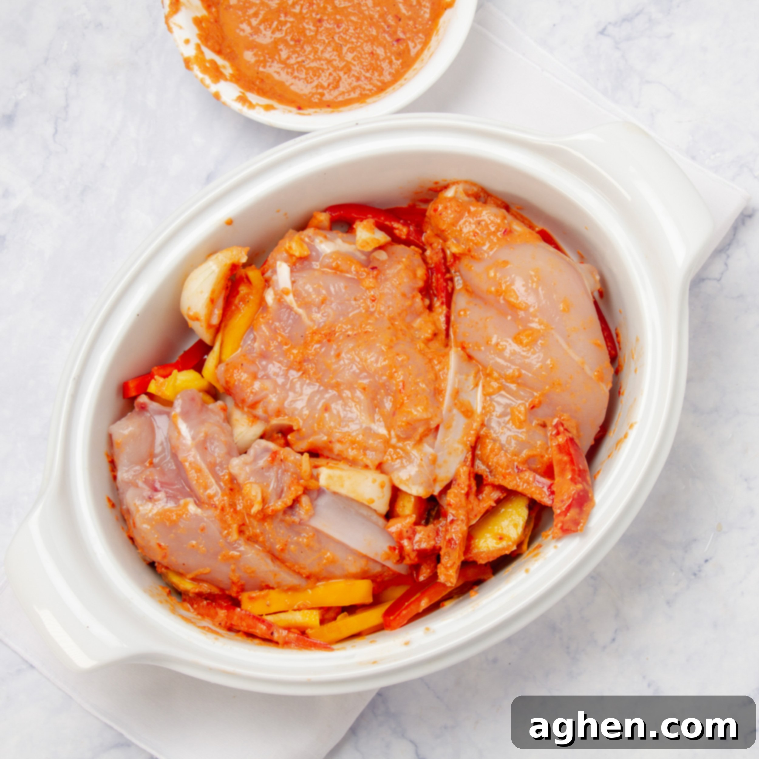 Marinated chicken, potatoes, and bell peppers coated in Piri-Piri sauce, spread evenly in a baking dish, ready for the oven.