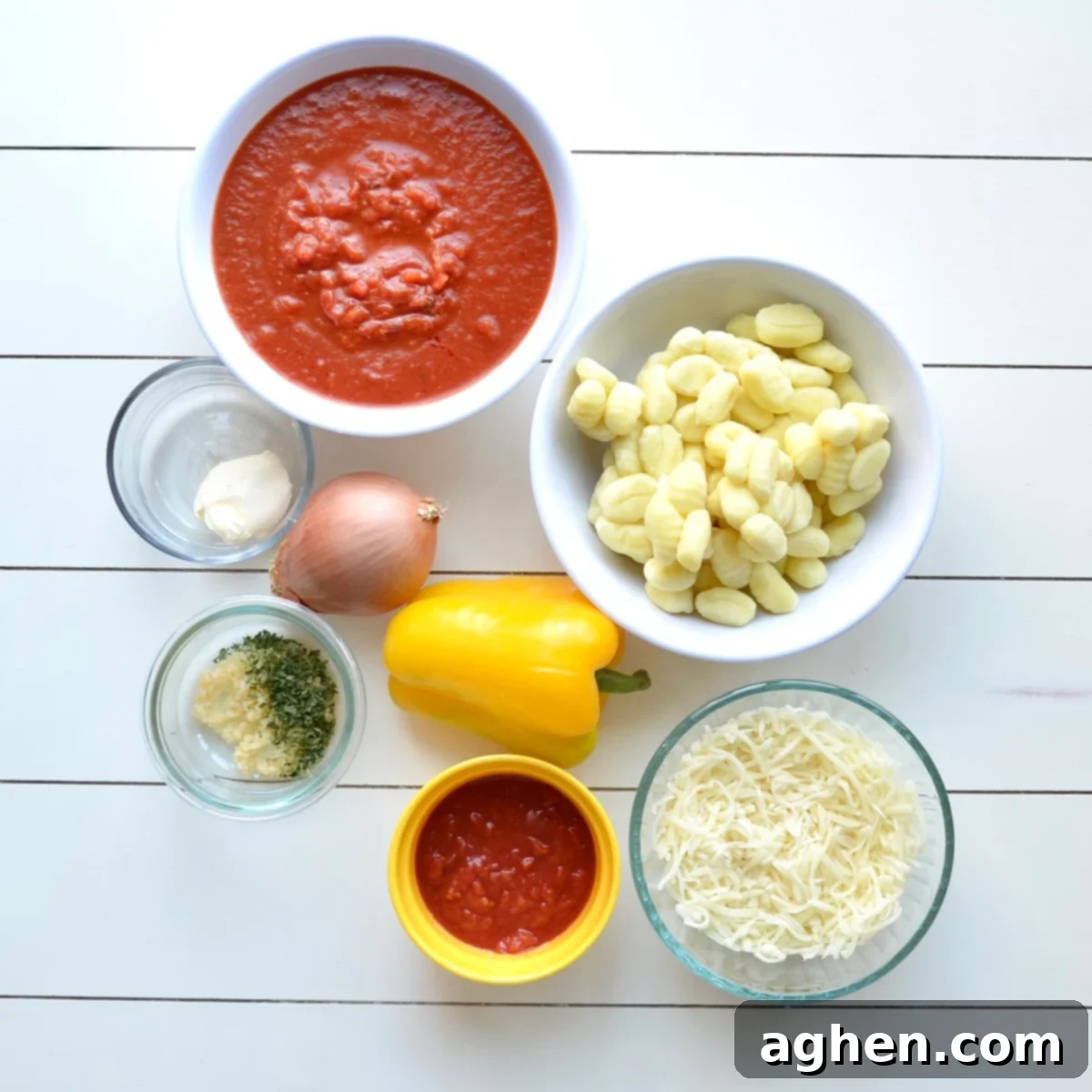 A selection of fresh ingredients laid out on a kitchen counter, including an onion, bell pepper, garlic cloves, a bag of potato gnocchi, and containers of crushed tomatoes and marinara sauce, all ready for making a cheesy gnocchi casserole.