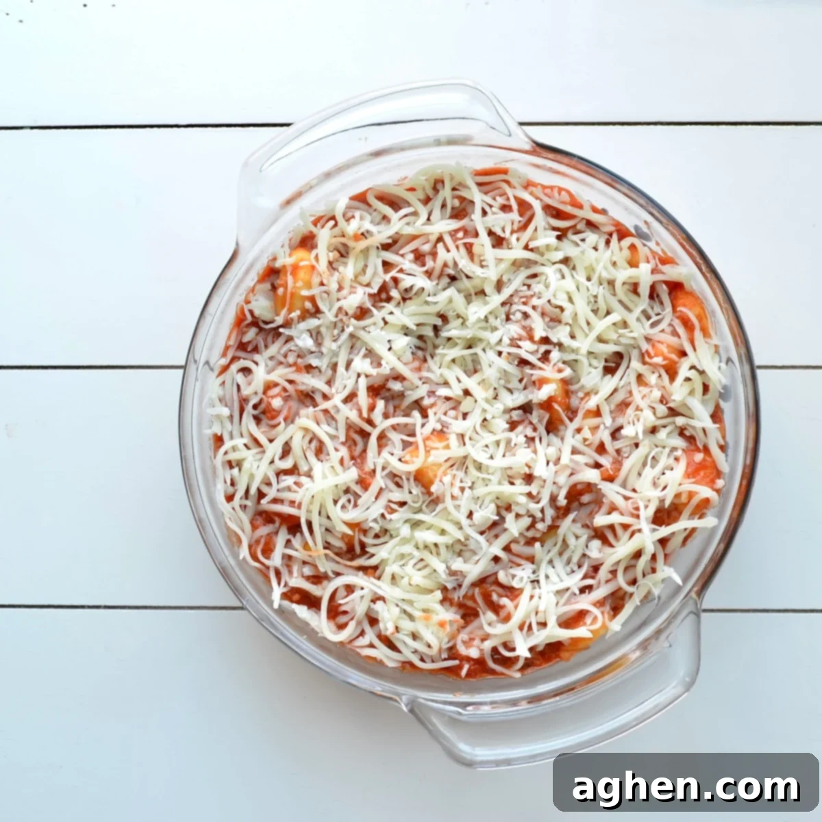 A baking dish filled with a pre-baked gnocchi casserole, topped with shredded mozzarella cheese, ready to be placed in the oven.