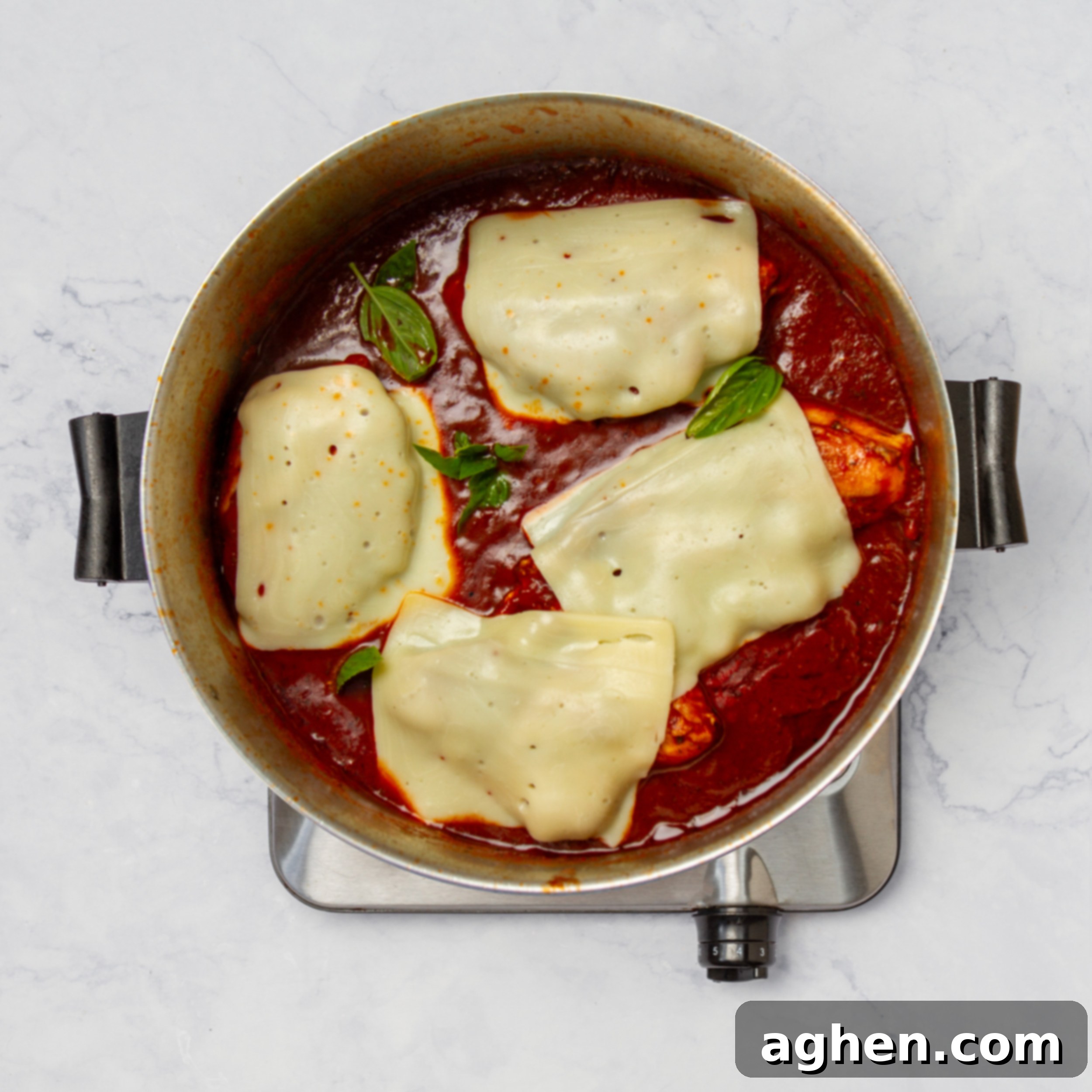 Cooked chicken in the pan, topped with melted mozzarella cheese and fresh basil, ready to be served.