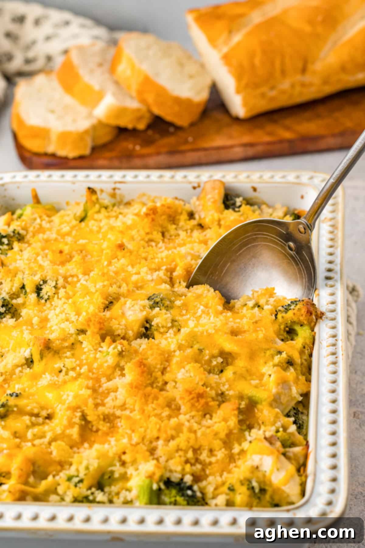 Serving spoon scooping out chicken divan from casserole dish. Sliced bread is in the background.