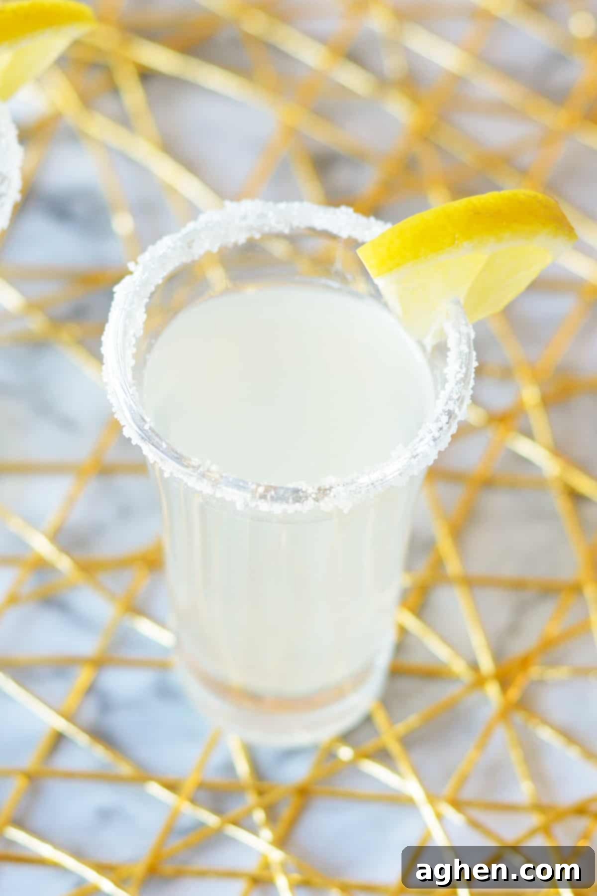 A single lemon drop shot in a 2-ounce glass with a sugar rim and a delicate lemon slice garnish, set against a blurred background.