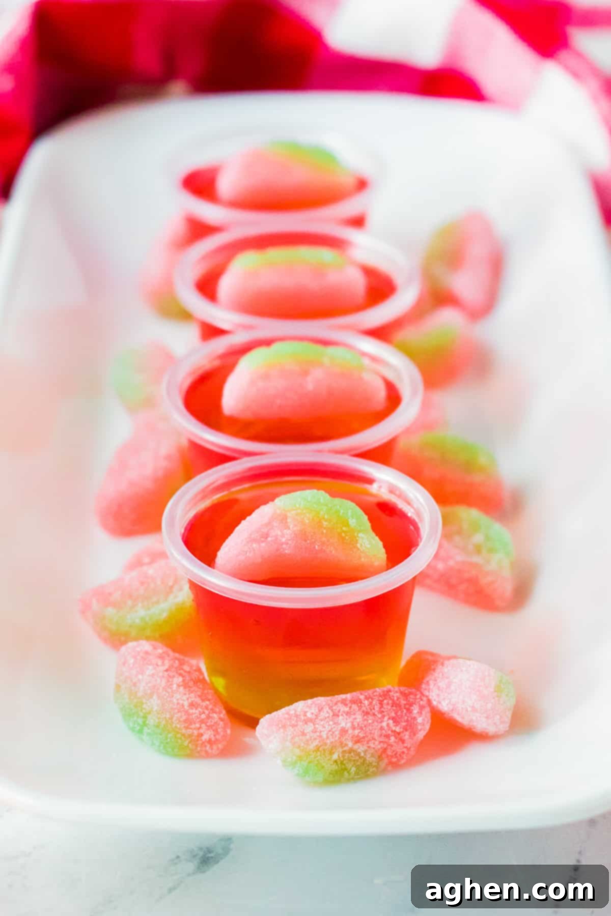 Watermelon vodka jello shots on white serving tray with watermelon sour candies around them.