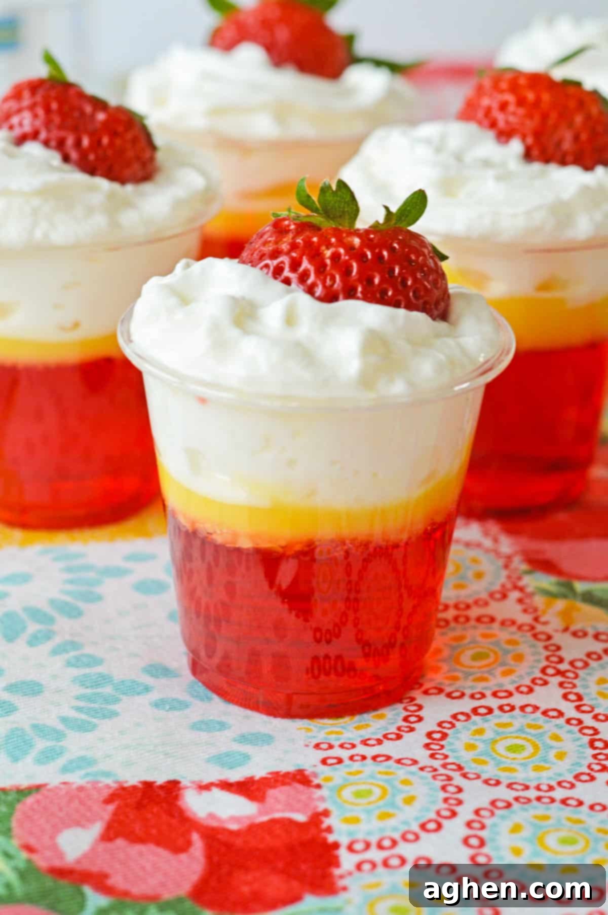 Strawberries and cream jello shots with 3 distinct layers: Strawberry jello, vanilla pudding, and whipped cream and topped with a fresh strawberry.