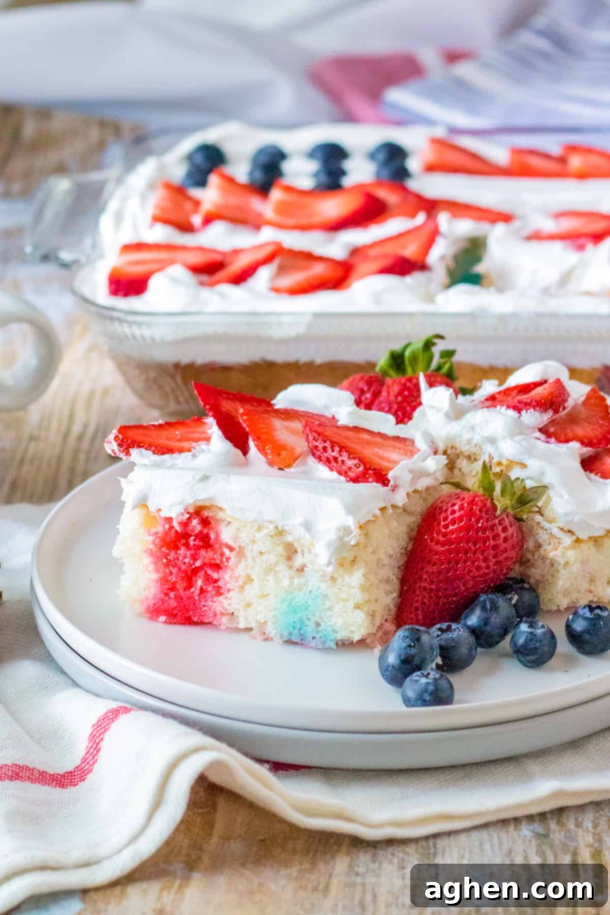 Stars and Stripes Poke Cake 2 4th of July poke cake with red and blue jello, cool whip topping, and fresh berries in the shape of a flag on top.