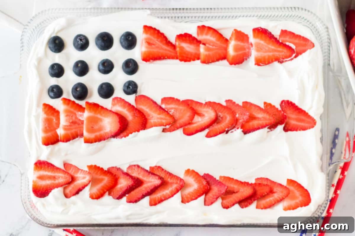 Stars and Stripes Poke Cake 3 Sheet cake topped with sliced strawberries and blueberries to resemble a flag.