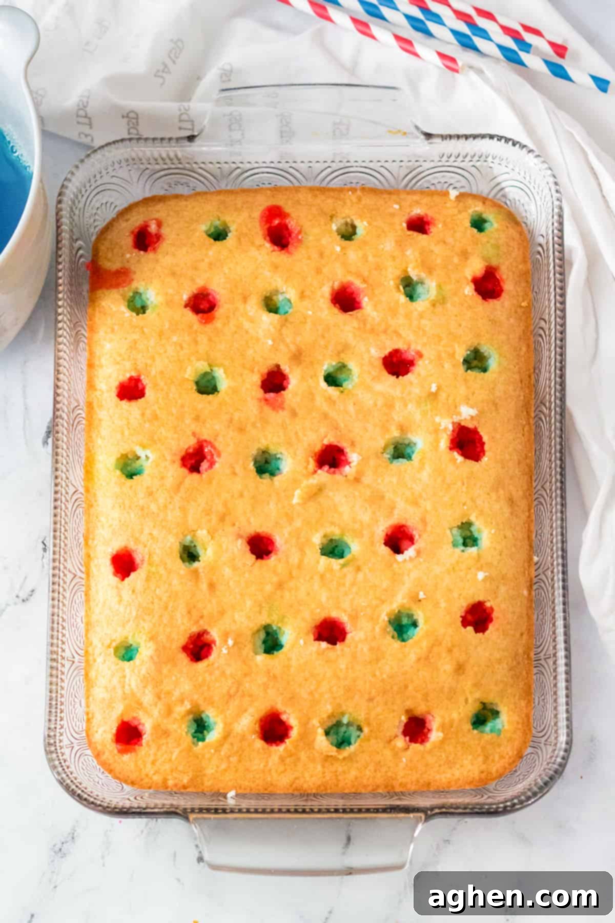 Golden cake with holes poked throughout the top and red and blue jello poured into alternating holes.