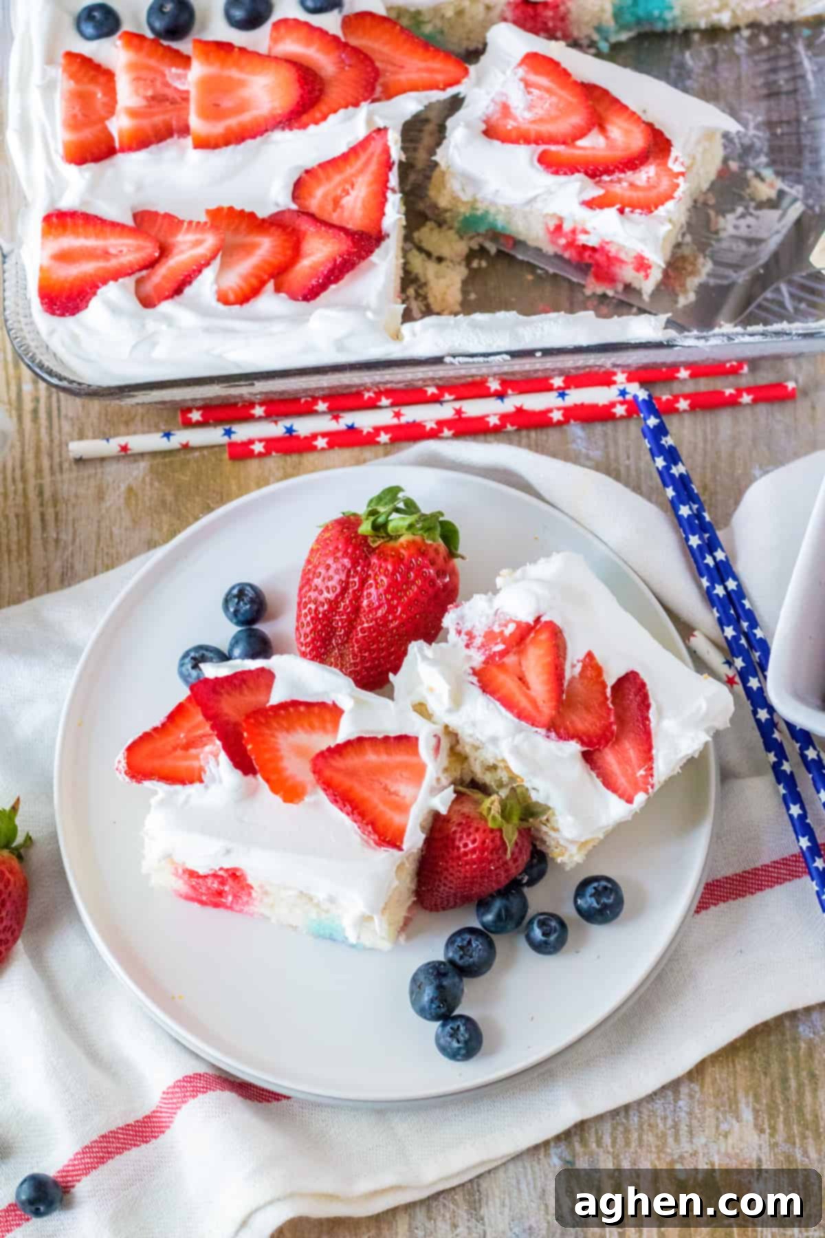 Stars and Stripes Poke Cake 9 4th of July flag cake topped with fresh fruit. Two slices are removed and placed on plate with fresh berries.