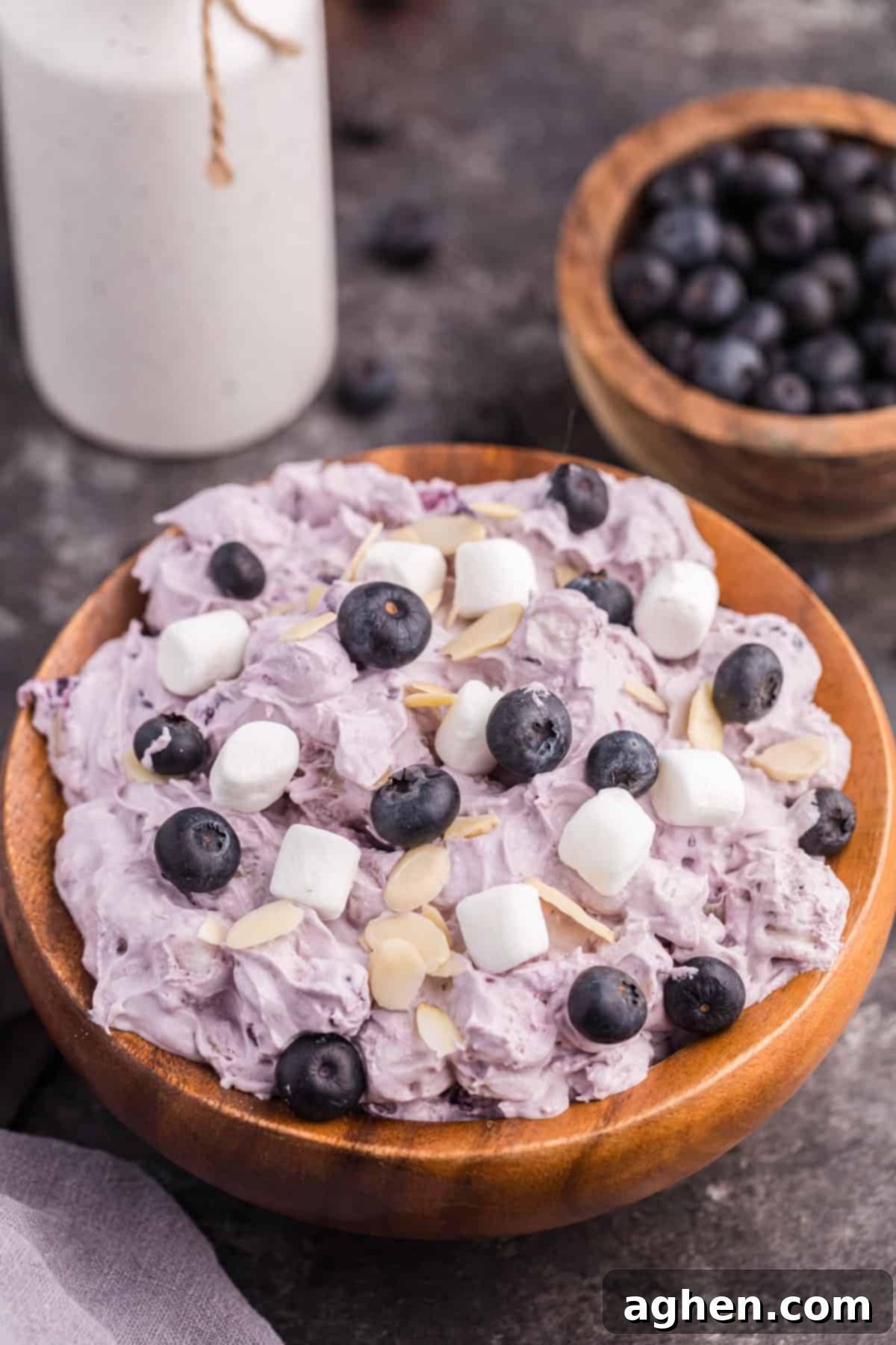 Blueberry fluff salad in a wooden bowl, topped with mini marshmallows, fresh blueberries, and almond slivers, ready to be served.